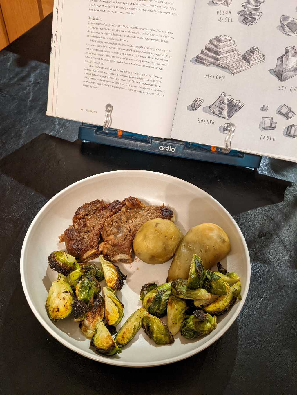 A meal of brussels sprouts, ribs, and sweet potatoes in front of a book