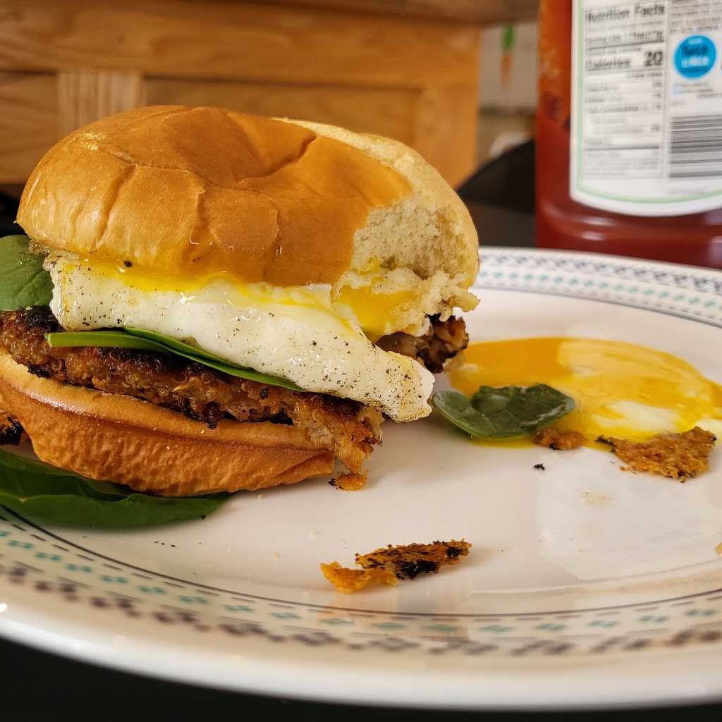 Closeup of a quinoa burger, after taking a bite out of it, causing the yolk to spill out