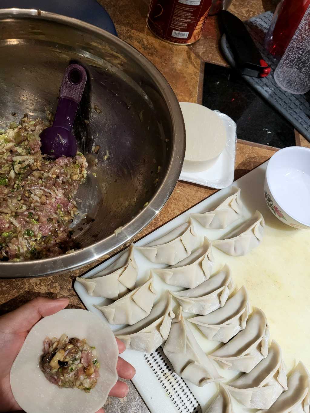 Dumpling preparation -- a bowl of the ground pork mixture, some wrapped dumplings, and in my hand, a dumpling wrapper with some filling.