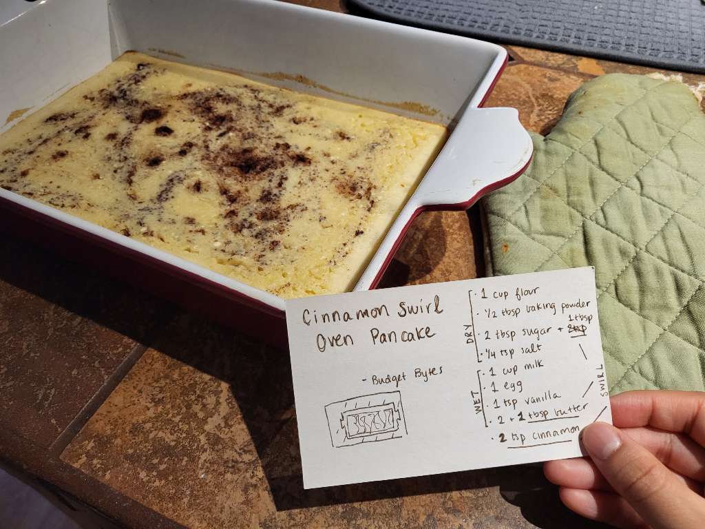 A large pancake in a baking pan, with a notecard next to it, showing the recipe