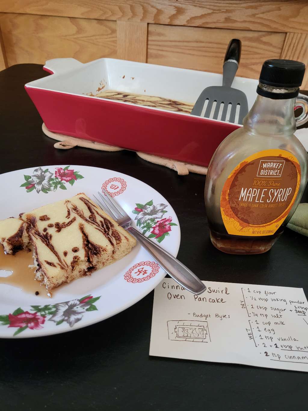 A piece of pancake on a plate, with some maple syrup on the side