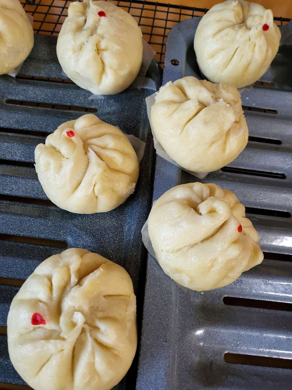 Cooked bao, each with a red dot, on some trays