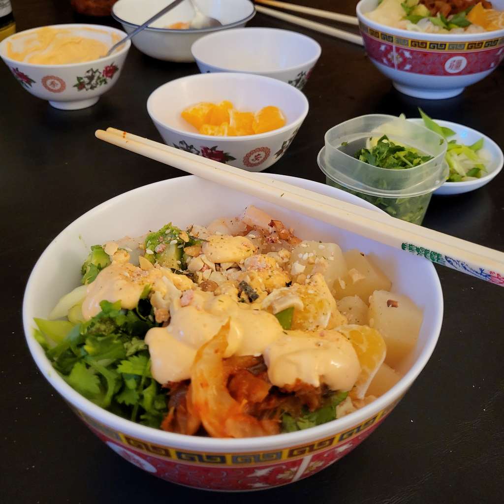 A bowl of shrimp poke with some of the toppings shown on the table