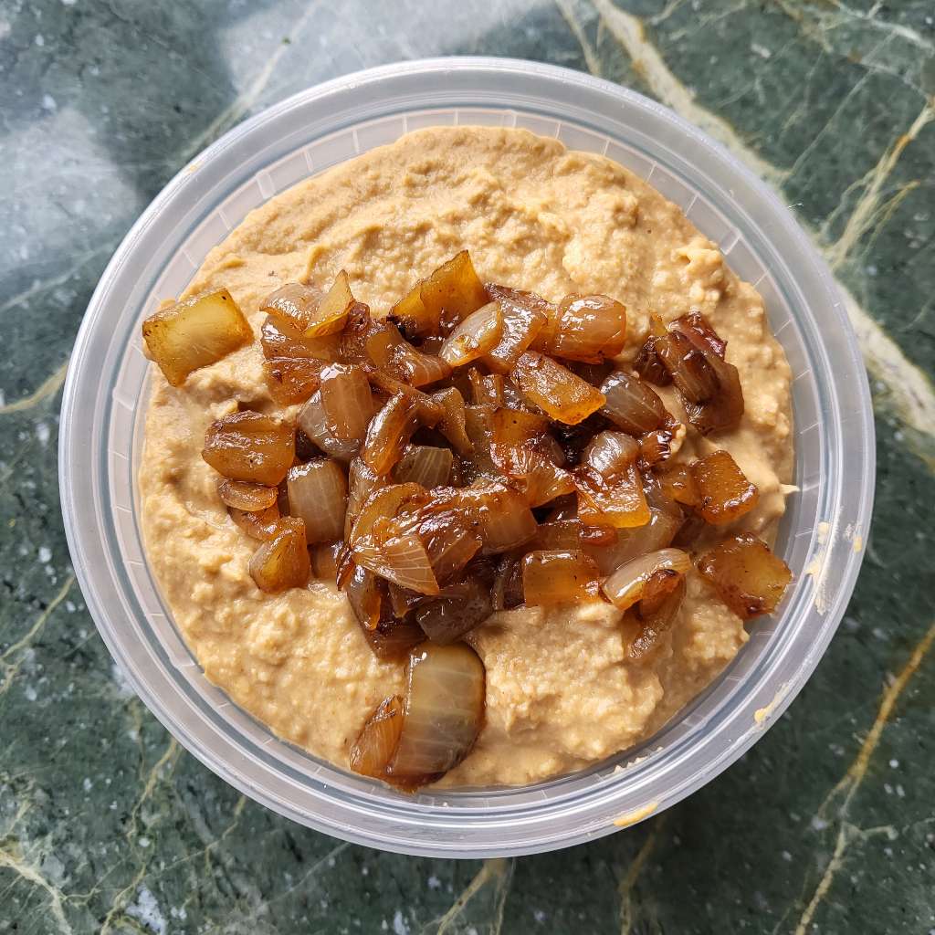 Caramelized onion and balsamic hummus, with more onions topped on it, in a container