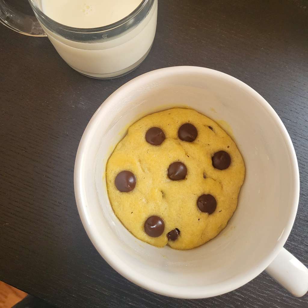 A chocolate chip cookie in a large mug, with some milk on the side