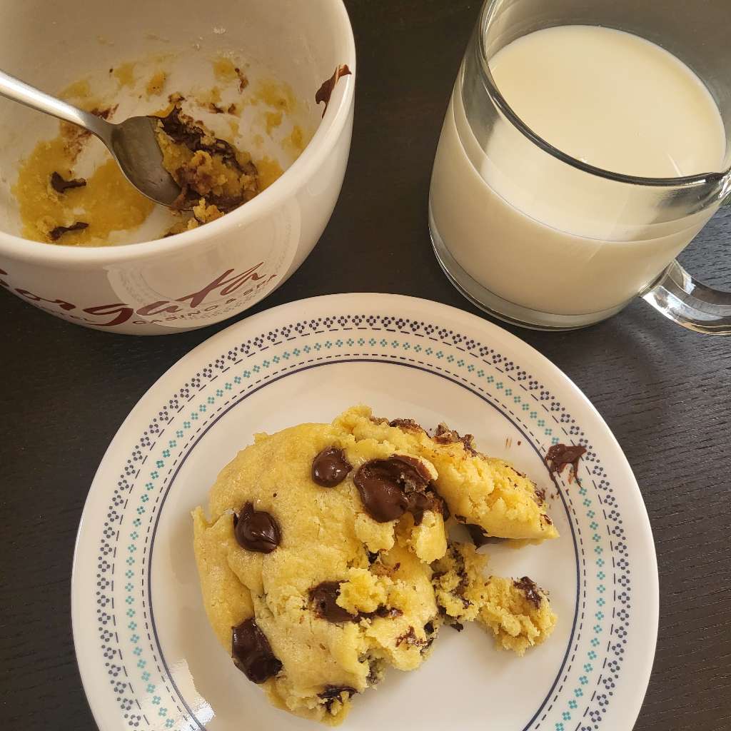 A chocolate chip cookie that was in a mug, but is now on a plate