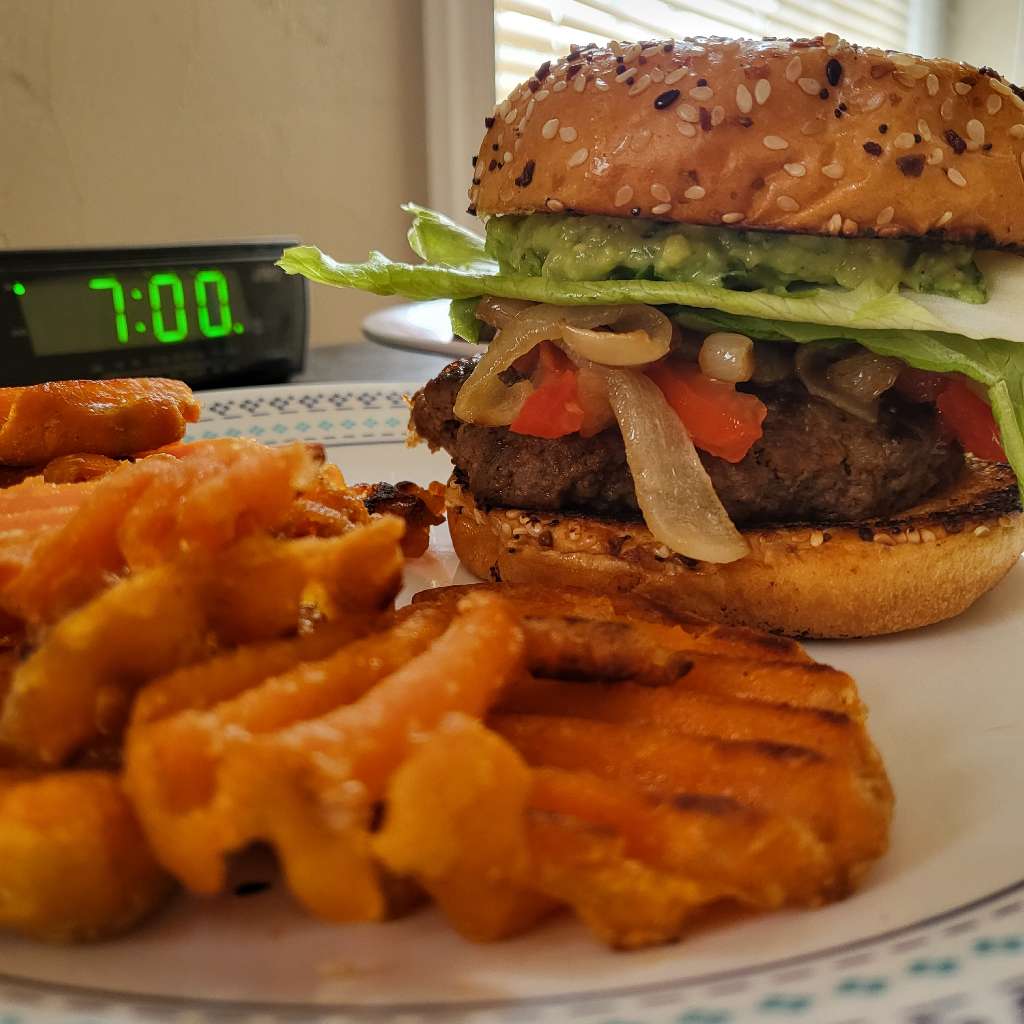 A burger and some waffle fries, sitting in front of a digital clock