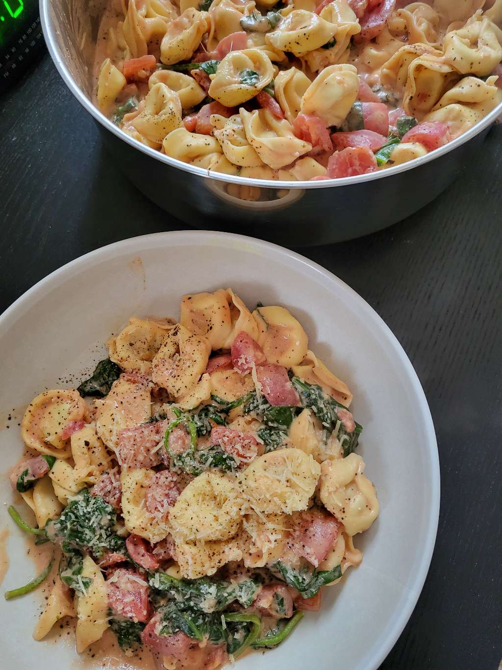 A bowl of tortellini pasta, next to the a pan of the same pasta