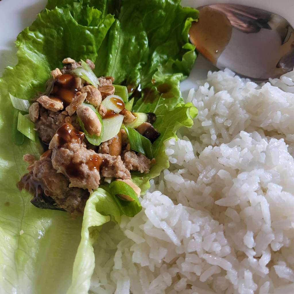 A scoop of the ground pork mixture on a lettuce leaf, with some rice next to it