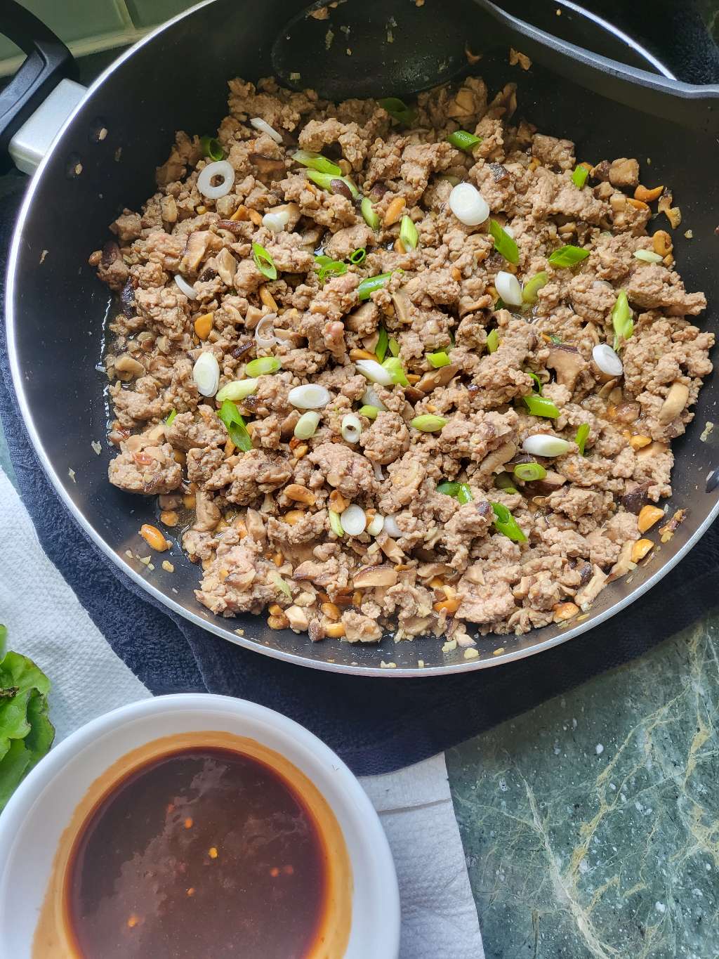 Some cooked ground pork in a pan next to some dipping sauce