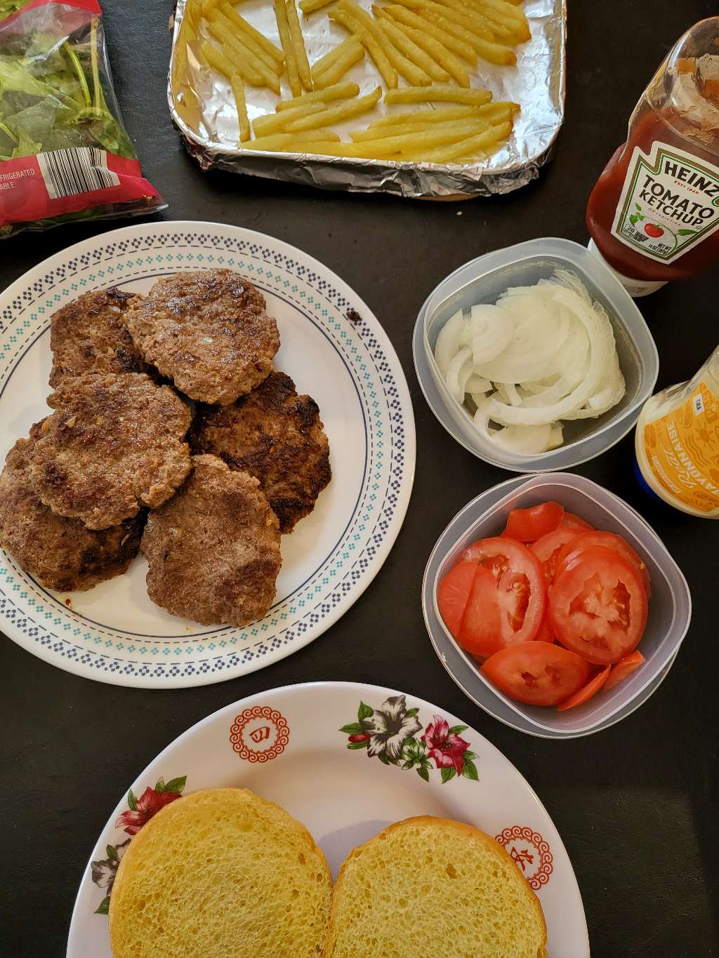 A top down view of all the burger components: spring mix, french fries, mayonnaise, ketchup, patties, tomato, onion, and a bun