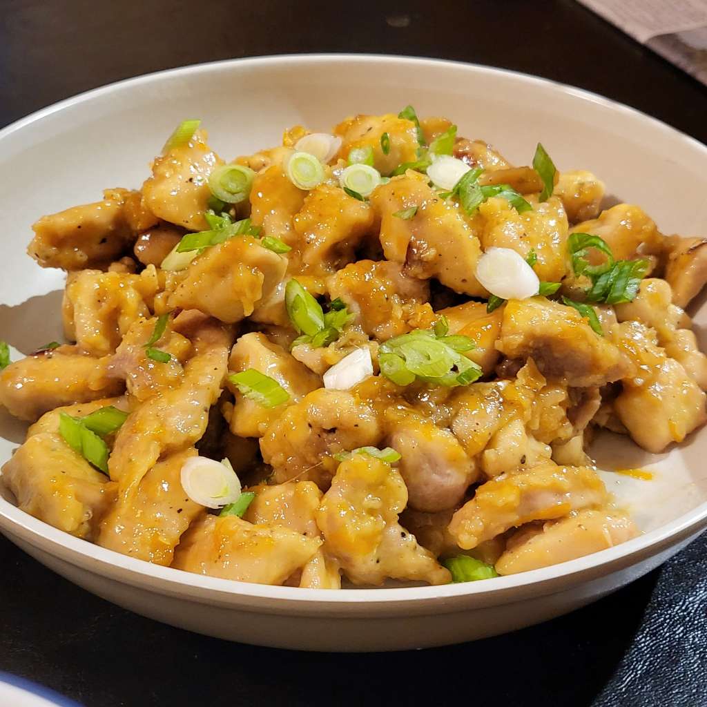 Close up of orange chicken, topped with scallion, on a plate