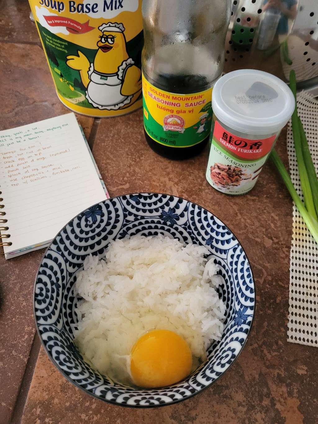 A raw egg and some rice in a bowl, with soy sauce, chicken bouillon powder, and furikake in the back