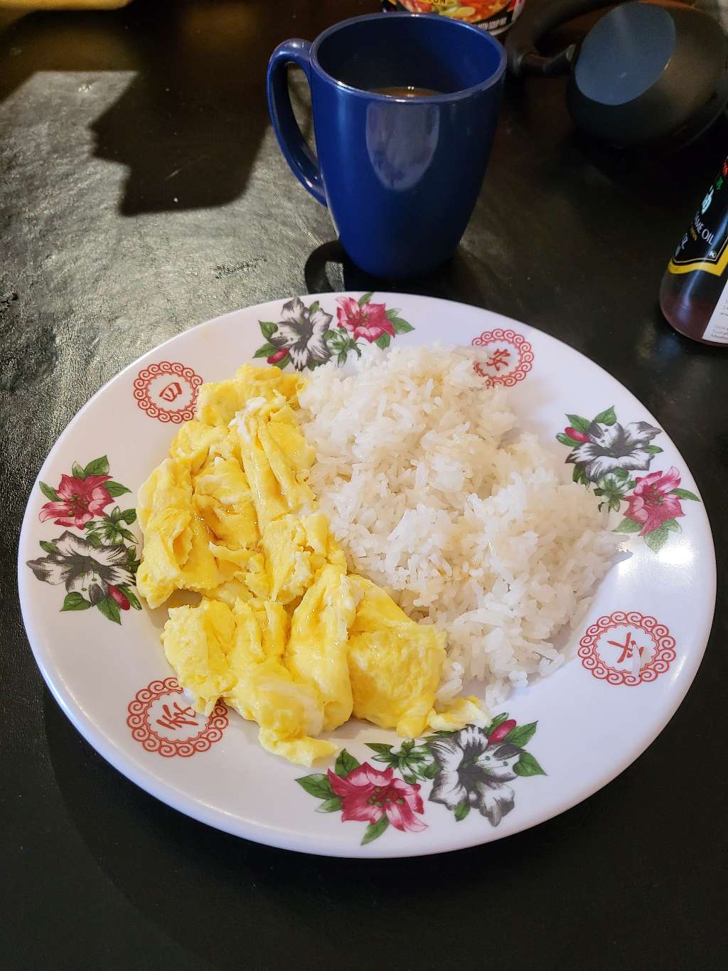 Scrambled eggs with rice, with sesame oil drizzled on top. There is also a cup of coffee in the back