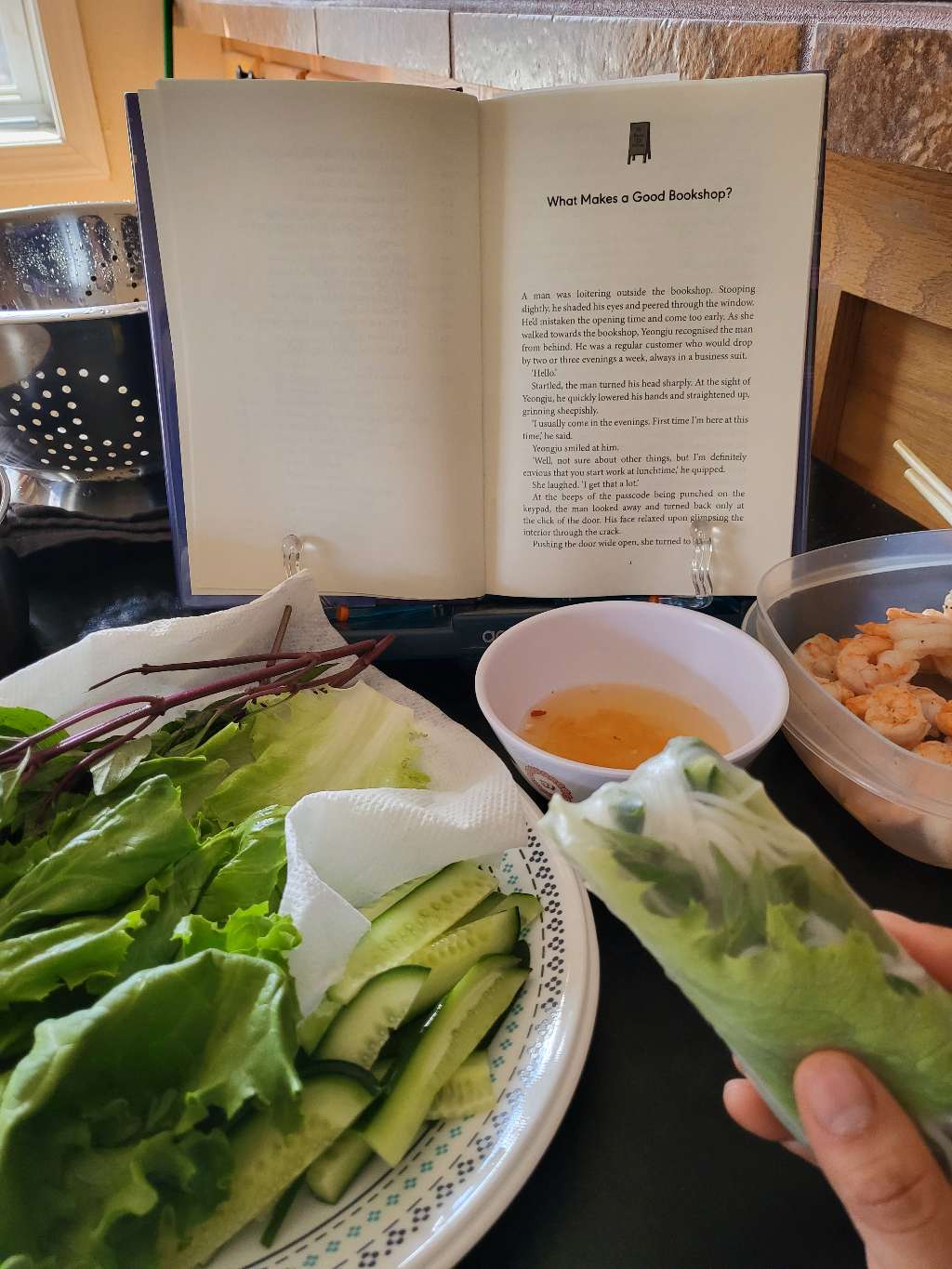 Holding a spring roll and also reading a book. Other spring roll ingredients are in the background as well