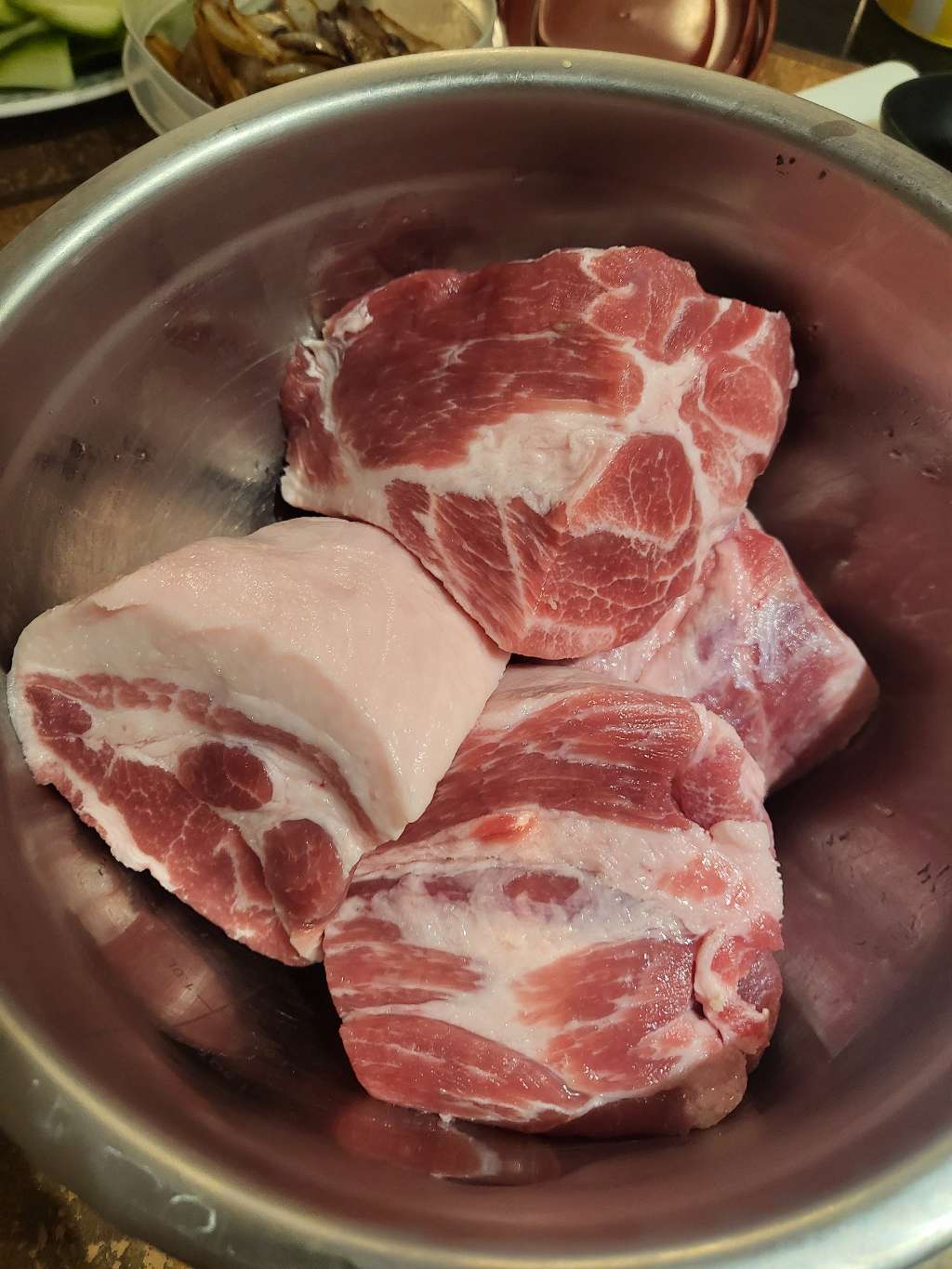 Some large chunks of uncooked pork butt in a bowl