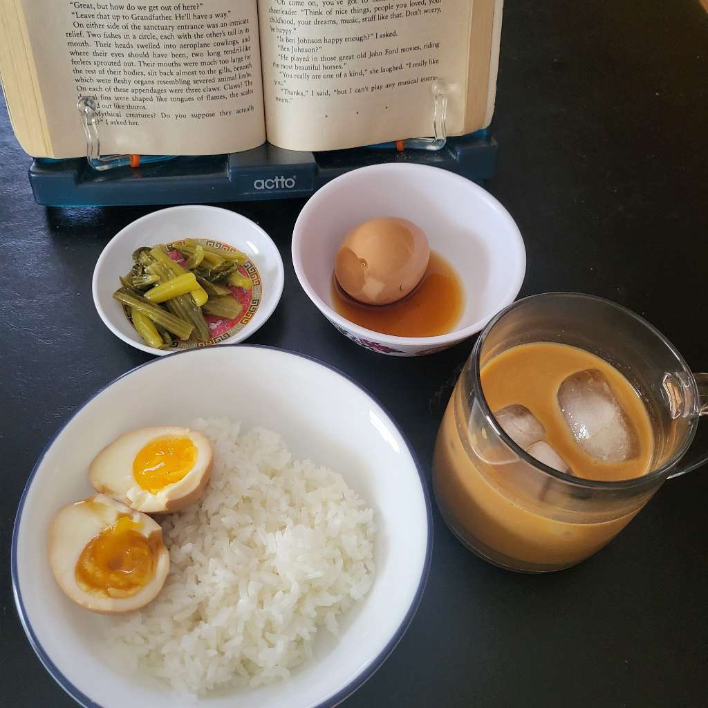Some marinated eggs, pickled mustard greens and rice. There is also iced coffee in a mug and a book in the back