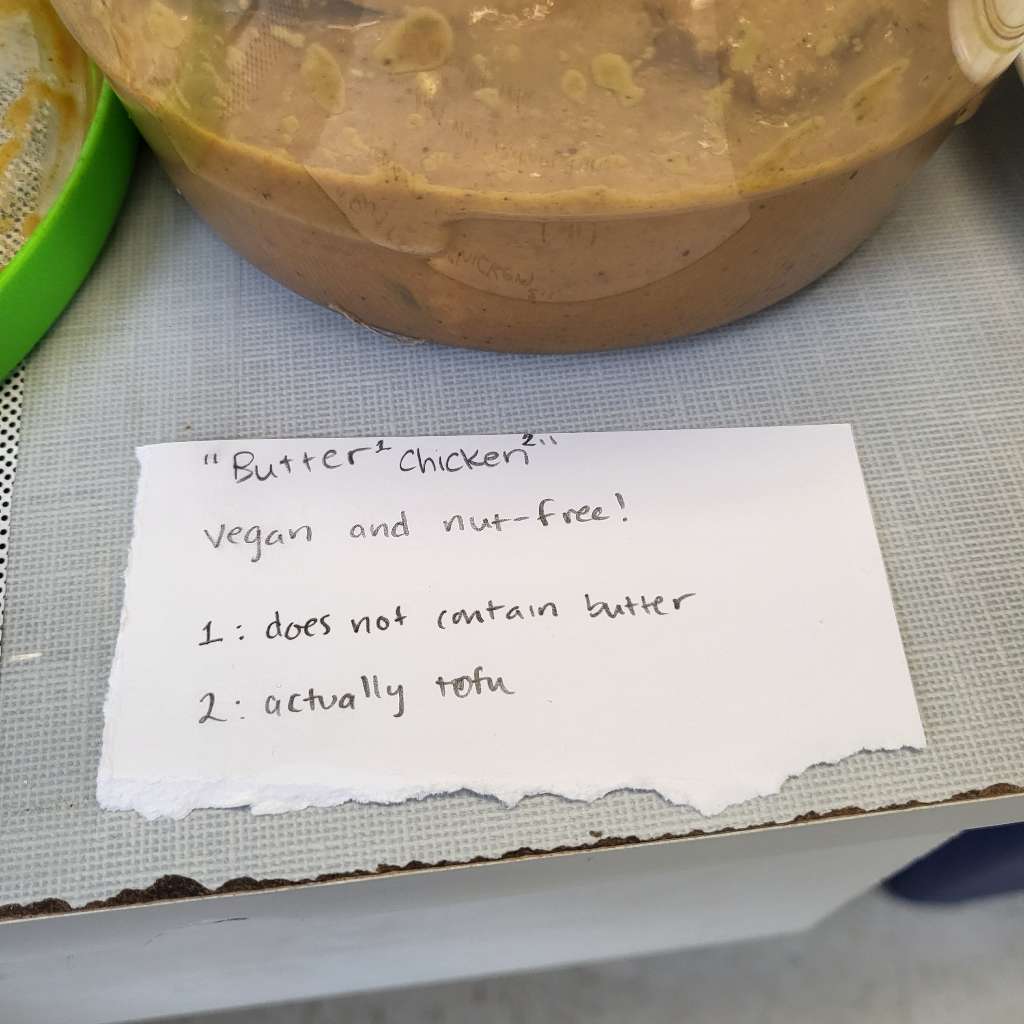 A sign that says "Butter chicken: vegan and nut free!" with my butter tofu behind it