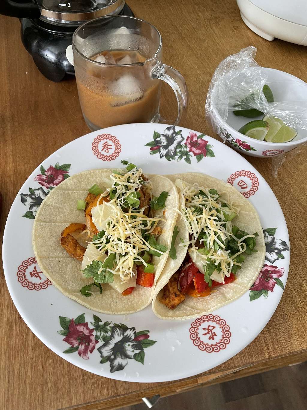 Two tacos with chicken and fajita veggies, along with an iced coffee and some lime wedges