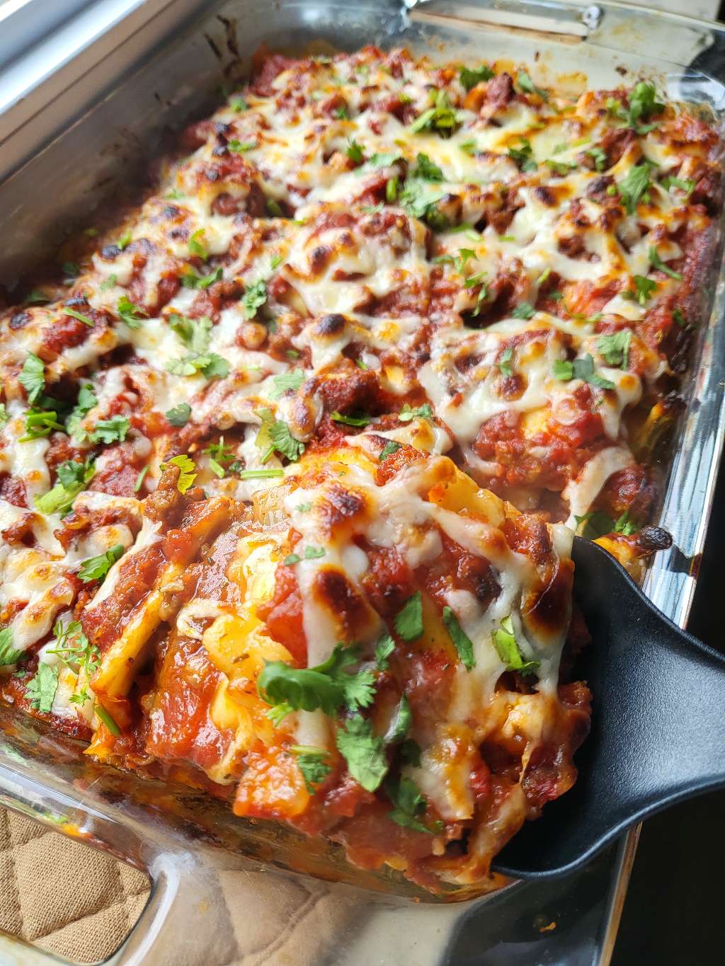 Baked ravioli sitting on a windowsill, with a spoon taking a piece out of it