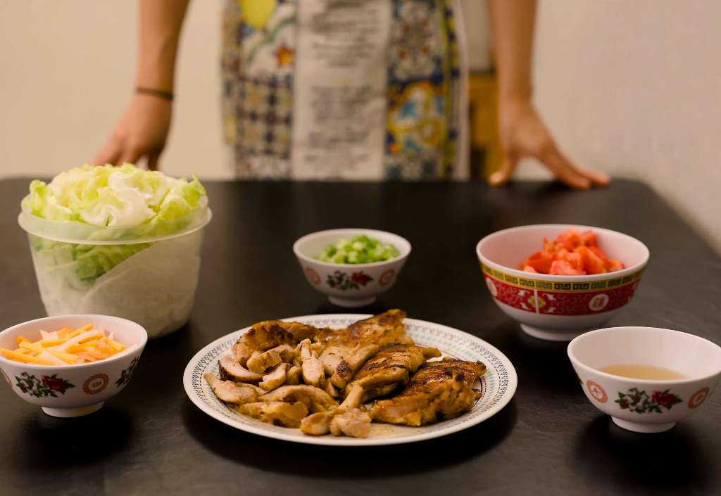 A dramatic shot of some Vietnamese style chicken, pickled veggies, lettuce, scallions, tomatoes, and fish sauce