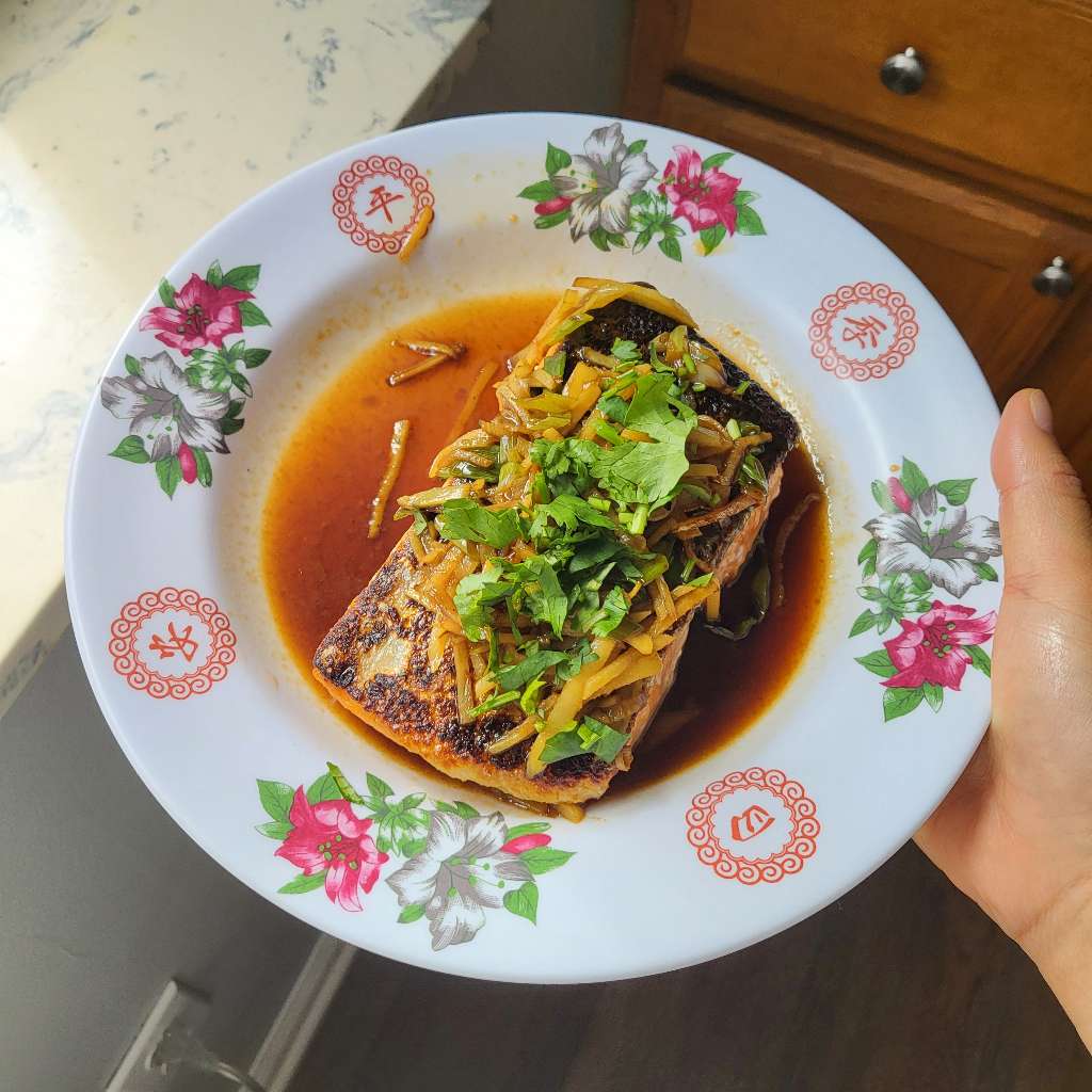 My hand holding up a plate of cooked salmon. This was from my second attempt
