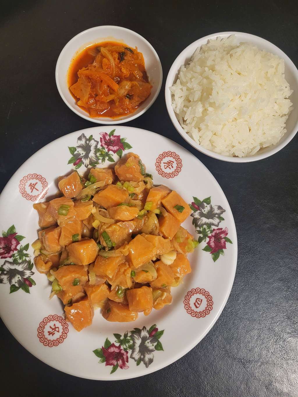 A plate of salmon poke, a saucer of kimchi, and a bowl of rice on the table