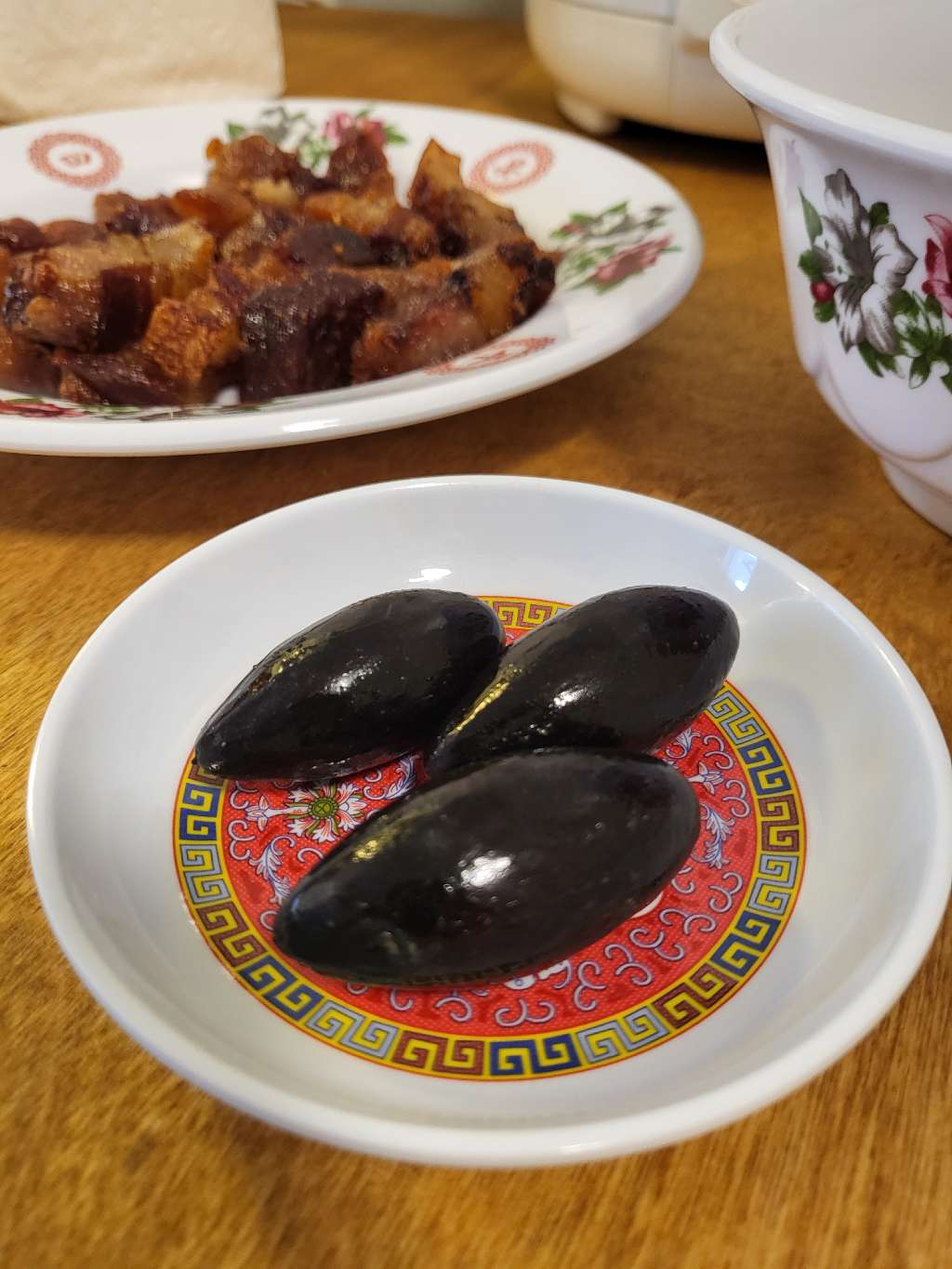 Three black olives in a saucer with some cured meat bits in the back