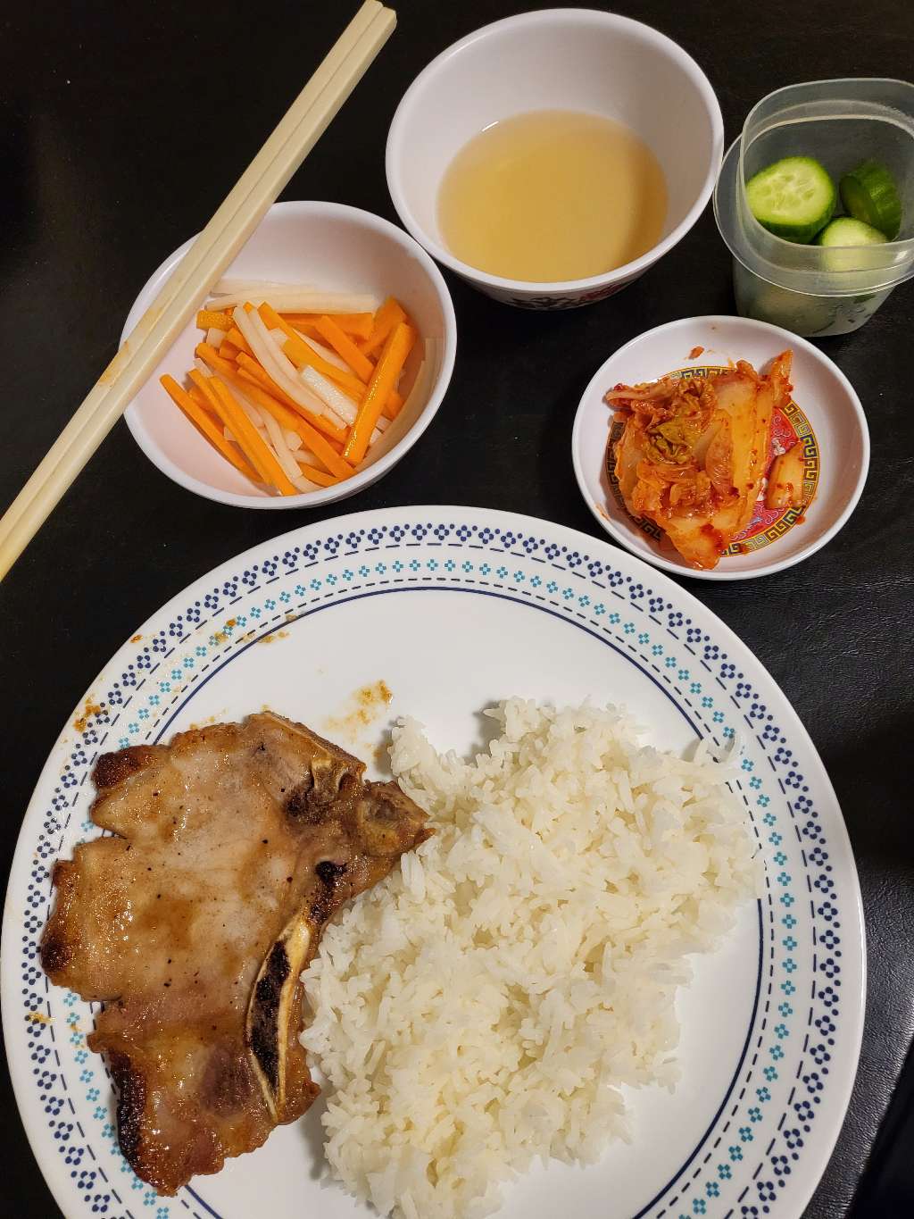 A pale pork chop with some rice, fish sauce, pickled carrot and daikon, kimchi, and cucumber